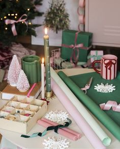 a table topped with lots of presents and christmas decorations next to a lit candle on top of a box