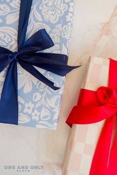 two wrapped gift boxes with blue and red ribbons on them sitting next to each other