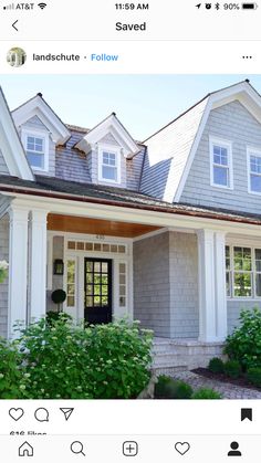 a gray house with white trim on the front door and two story windows, along with green shrubs