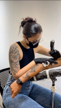 a woman with tattoos on her arm sitting at a table and holding a camera in front of her