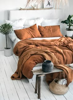 a bed with an orange comforter and pillows on top of it in a white room