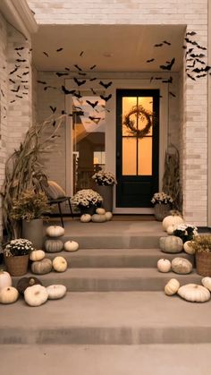 a front porch decorated for halloween with pumpkins and decorations on the steps, bats flying overhead