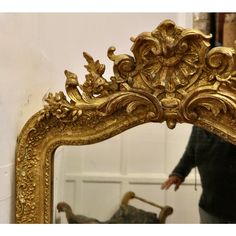 a person standing in front of a mirror with an ornate gold frame on the wall