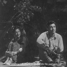 an old photo of two people sitting next to each other in front of a tree