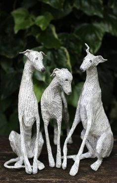 three small white animals sitting next to each other on top of a wooden table with plants in the background