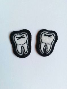 two black and white tooth shaped patches on a white surface, with one showing the teeth