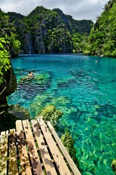 the water is crystal blue and clear with some people swimming in it at the bottom