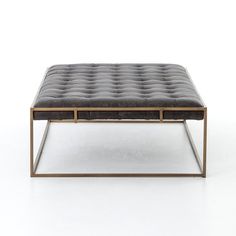 a black leather ottoman with gold frame and metal legs on a white background, viewed from the front