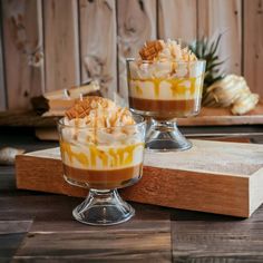 two glasses filled with dessert sitting on top of a wooden table