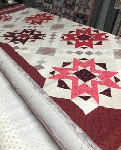 a quilted table topper with red and white stars on it, sitting on a bed