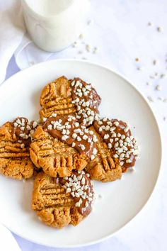 a white plate topped with cookies covered in chocolate and sprinkles next to a glass of milk