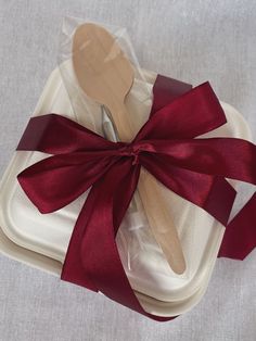 a wooden spoon sitting on top of a white plate covered in red ribbon and bow