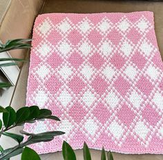 a pink and white crocheted blanket sitting on top of a table next to a potted plant