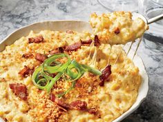 a bowl filled with macaroni and cheese topped with green onions, bacon and melted cheese