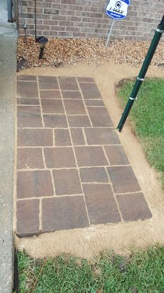 a brick walkway in front of a house with grass around it and a street sign on the sidewalk