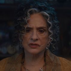 a close up of a person with curly hair and an earring in front of a dark background