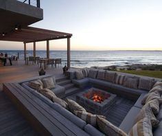 an outdoor seating area with fire pit and ocean in the background at sunset or dawn