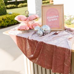 a table topped with pink donuts next to a sign and other food on top of it