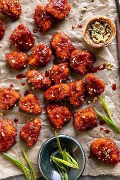 chicken wings with sauce and green onions on a sheet of parchment paper next to a small bowl of seasoning