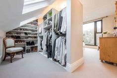 an attic closet with lots of clothes and shoes on the shelves in front of it