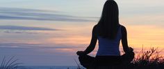 a woman is sitting in the grass with her back to the camera as the sun sets