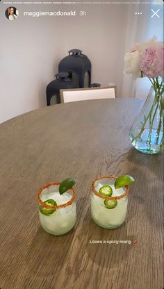 two glasses filled with cucumbers sitting on top of a wooden table next to a vase