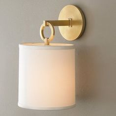 a wall light with a white shade on it's side and a gold ring around the lamp