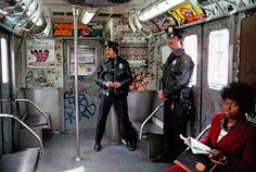 two police officers standing on the inside of a subway car with graffiti all over it