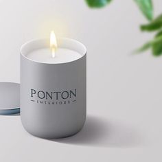 a candle that is sitting in front of a white cup with the word ponton interiors on it