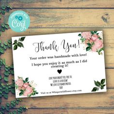 a thank card with pink flowers and greenery around it on a wooden surface, next to green leaves