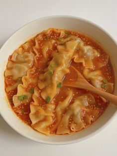 a white bowl filled with pasta and sauce on top of a table next to a wooden spoon