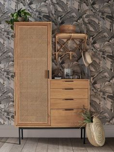 a wooden cabinet sitting in front of a wall with plants and hats on top of it