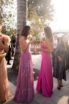 two women standing next to each other in front of a group of people wearing dresses