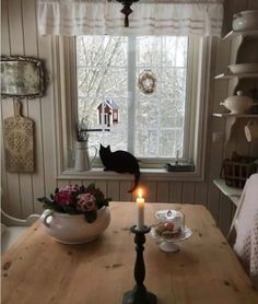 a cat sitting on the window sill next to a table with plates and cups