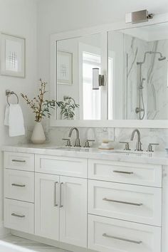 a white bathroom with marble counter tops and large mirrors on the wall above the sinks