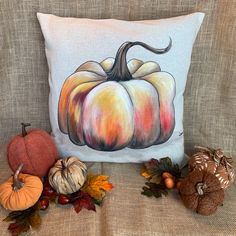 a pillow with a painted pumpkin on it next to other fall decorations and acorns