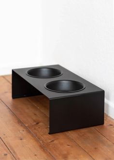 two black bowls sitting on top of a wooden floor next to a white wall and wood floor