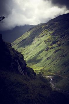 a mountain with green grass on the side and dark clouds in the sky