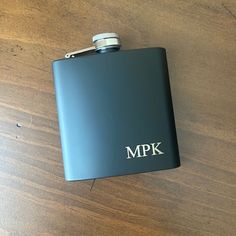 a black hip flask with the word mpk on it sitting on a wooden table