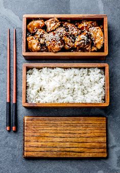 two wooden trays filled with rice and meat next to chopsticks on a table