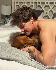 a shirtless man laying on top of a bed next to a small brown dog