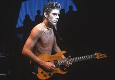 a shirtless man with white paint on his face and neck playing an electric guitar