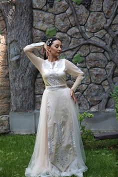 a woman in a white dress standing on grass with her hands behind her head and wearing a tiara