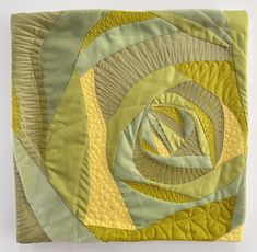 a green and yellow quilted wall hanging on a white wall with a circular design