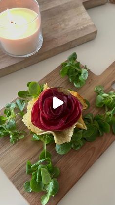 a wooden cutting board topped with a beet and leafy vegetable sandwich next to a candle