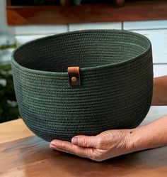 a person holding a large green basket on top of a wooden table