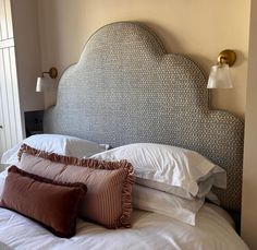 a bed with white sheets, pillows and a headboard made out of an upholstered fabric