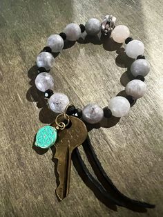 a bracelet with two charms and a key on top of the beaded bracelet is sitting on a wooden surface