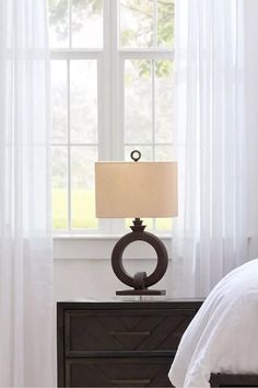 a bedroom scene with focus on the nightstand and lamp beside it, while the bed is covered in white drapes