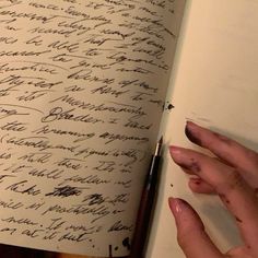 a hand holding a pen over a book with writing on the pages in cursive ink